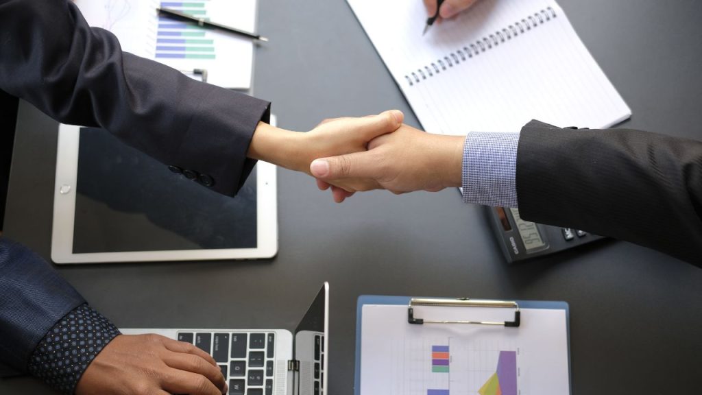 Deux professionnels se serrent la main au-dessus d'un bureau avec des outils de travail, symbolisant un accord de crédit professionnel.