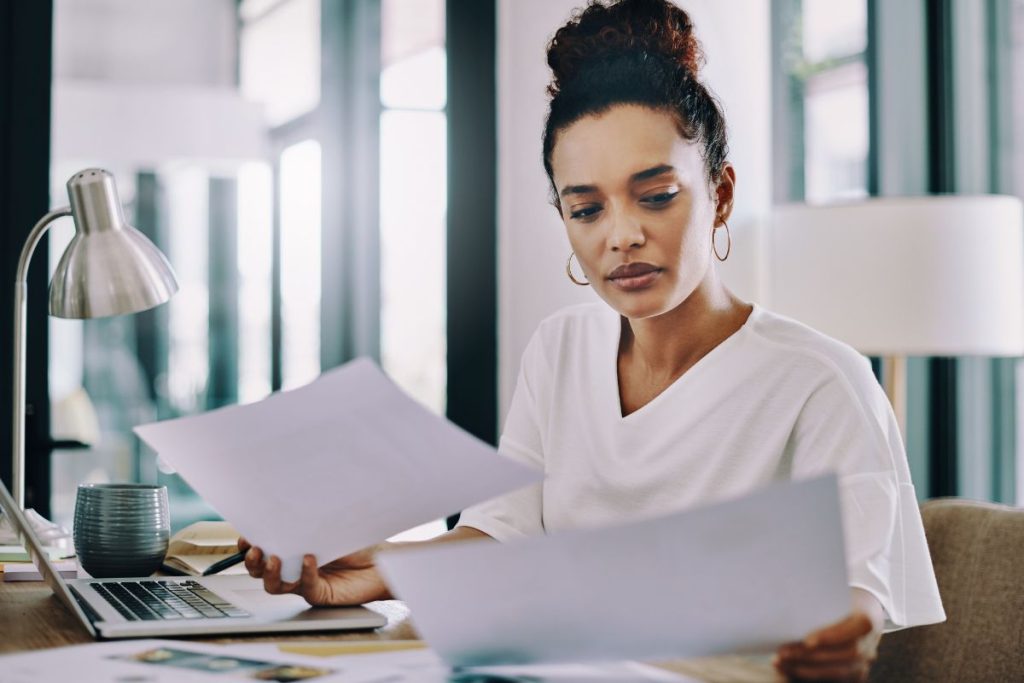 Femme examinant des documents à son bureau, traitant le changement d'adresse pour son statut d'auto-entrepreneur.